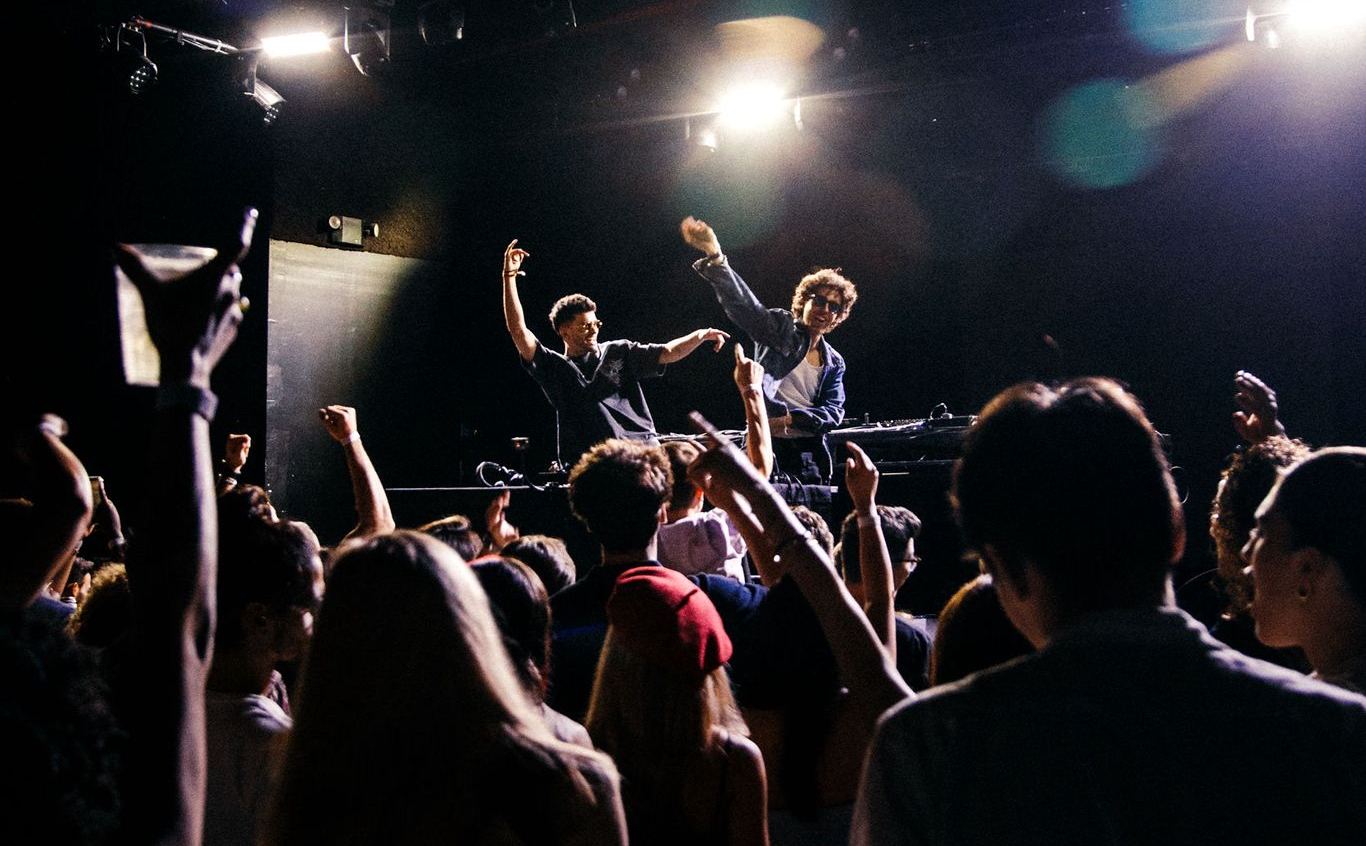 tradeoff on stage at Racket, arms up over a packed crowd
