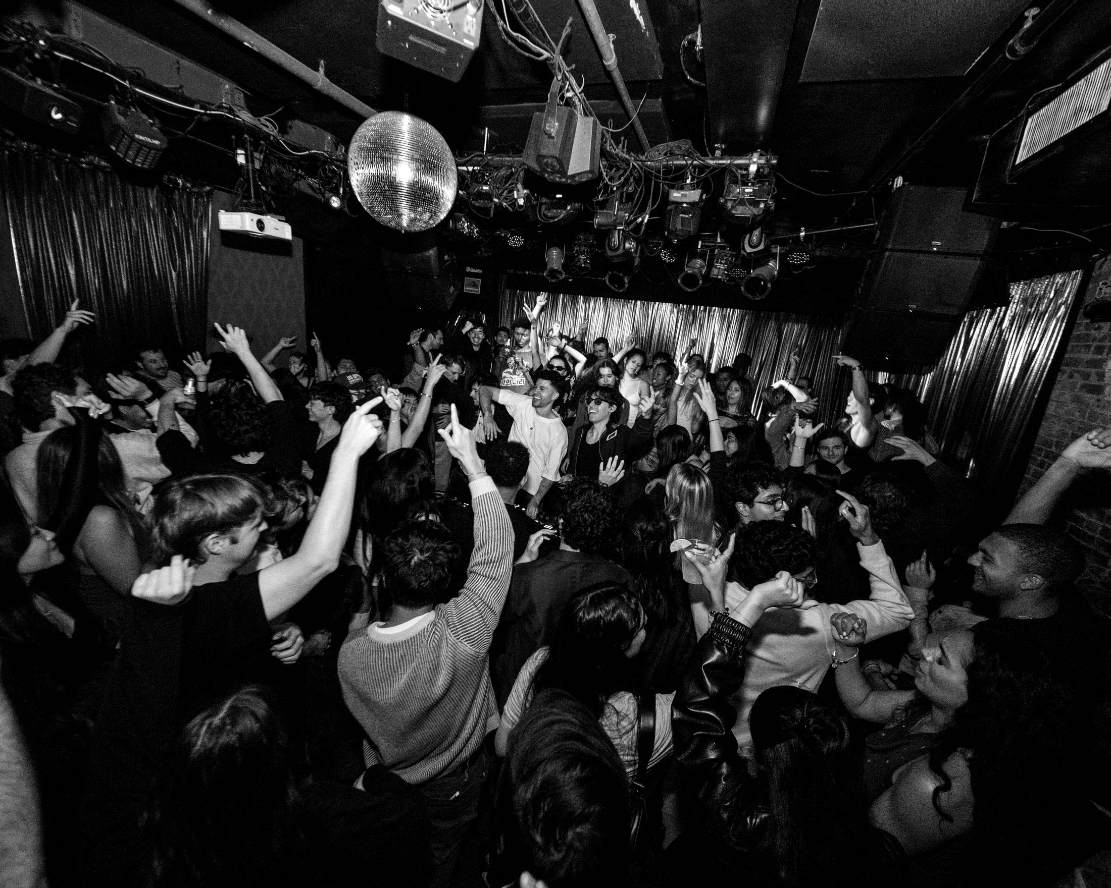 A packed room with hands in the air under a disco ball during a tradeoff set
